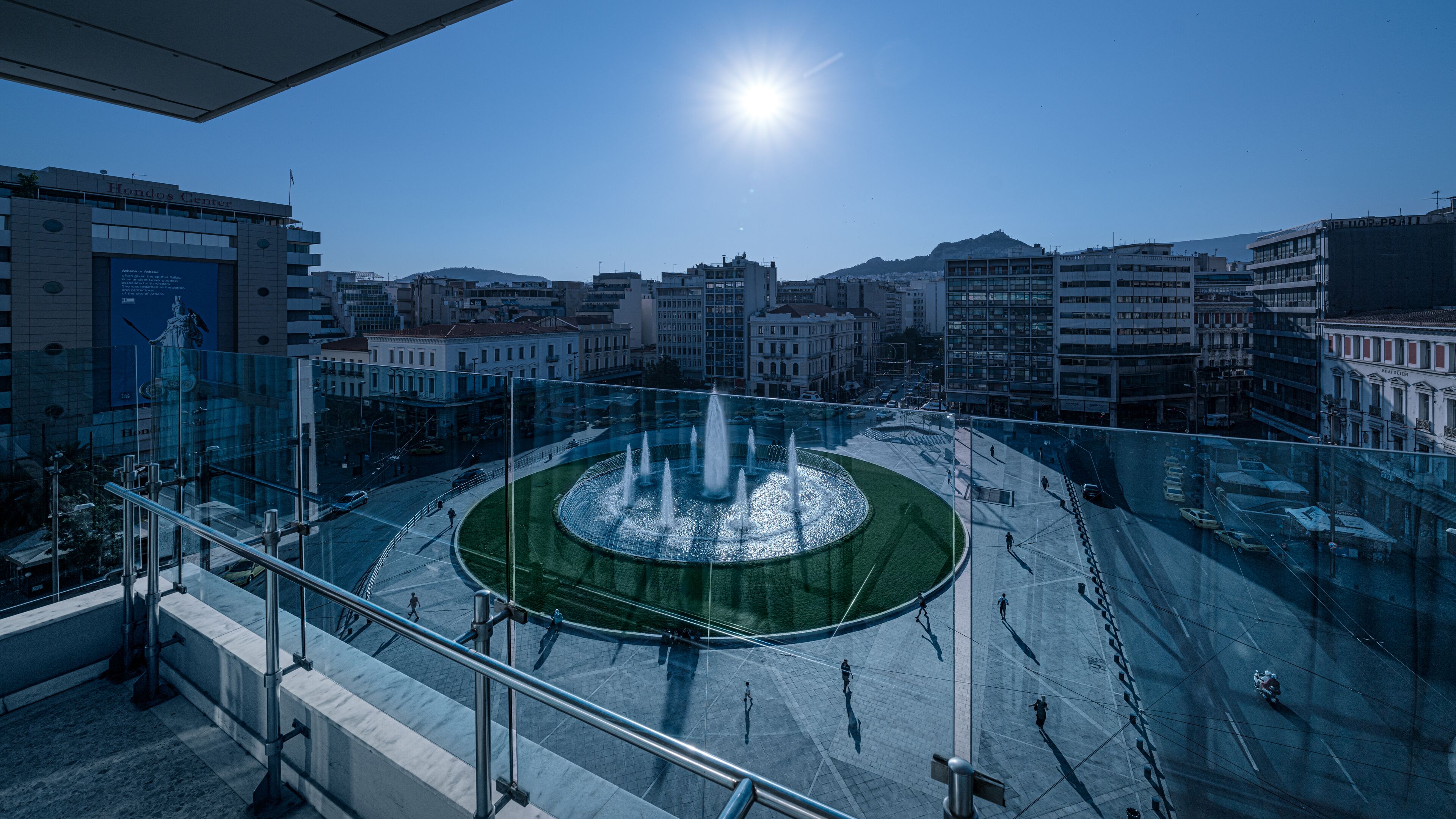 A plaza with a fountain, surrounded by buildings and a clear sky.