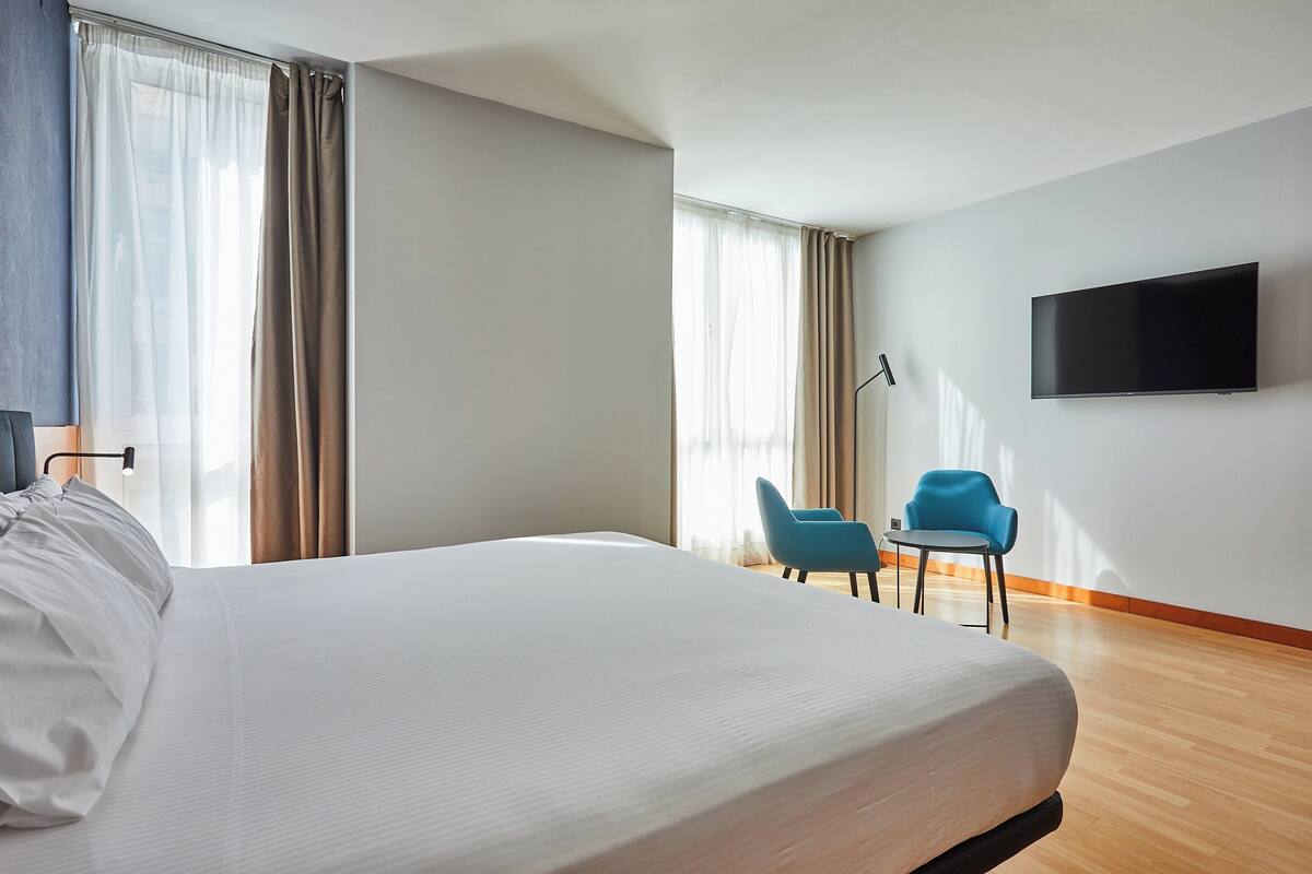 A hotel room with a large bed, a flat-screen TV mounted on the wall, and two chairs.