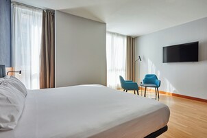 A hotel room with a large bed, a flat-screen TV mounted on the wall, and two chairs.