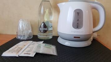 Une bouilloire électrique blanche, une bouteille en verre avec une étiquette et des sacs en plastique sur un tapis noir.