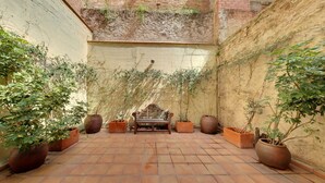 Une cour avec un banc, des plantes en pot et un sol carrelé.