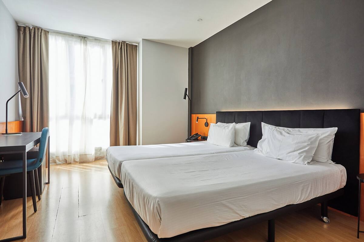 A hotel room with two beds, a desk, and a chair.