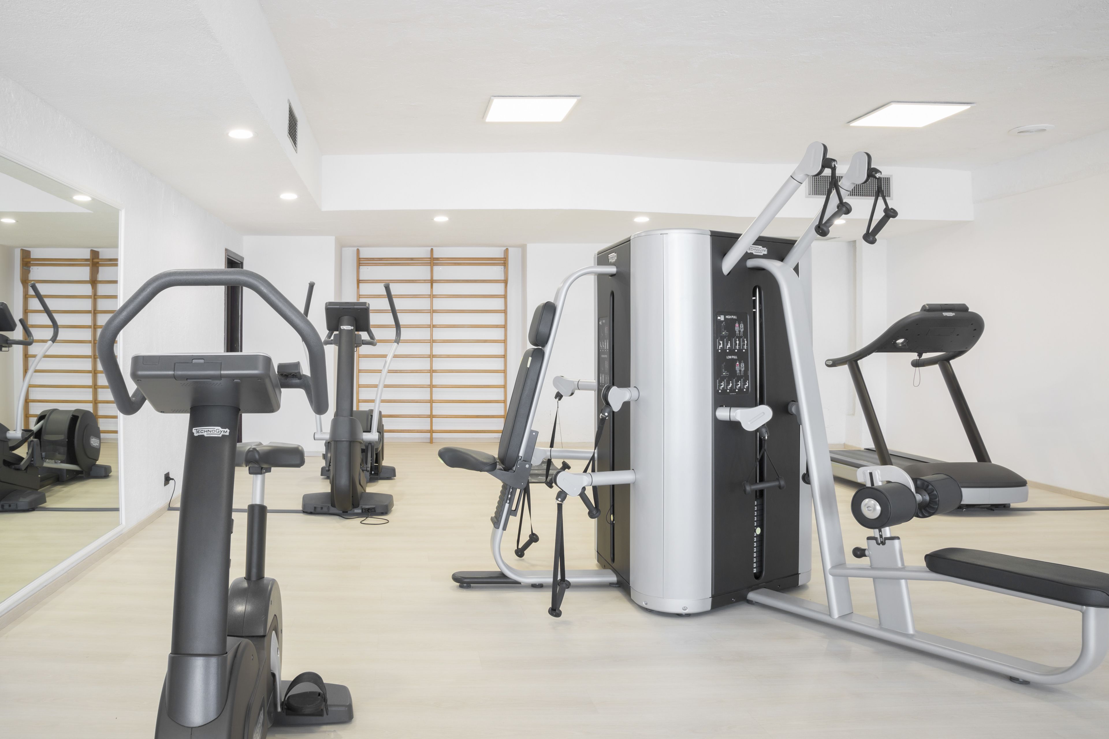 Ein Fitnessstudio mit verschiedenen Trainingsgeräten, darunter Laufbänder, ein Crosstrainer und Kraftgeräte.