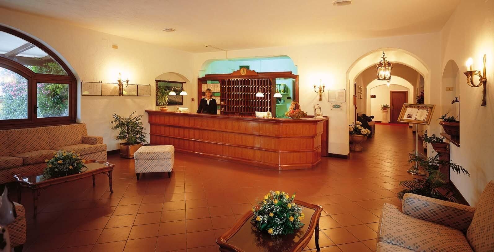 A hotel lobby with a reception desk, sofas, a coffee table, and a staircase leading to another area.