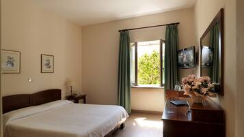 Habitación de hotel con cama, escritorio con espejo, televisión y ventana con cortinas.