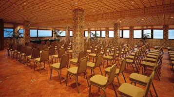 Une salle de conférence avec des rangées de chaises, une scène avec un pupitre et de grandes fenêtres donnant sur l’océan.