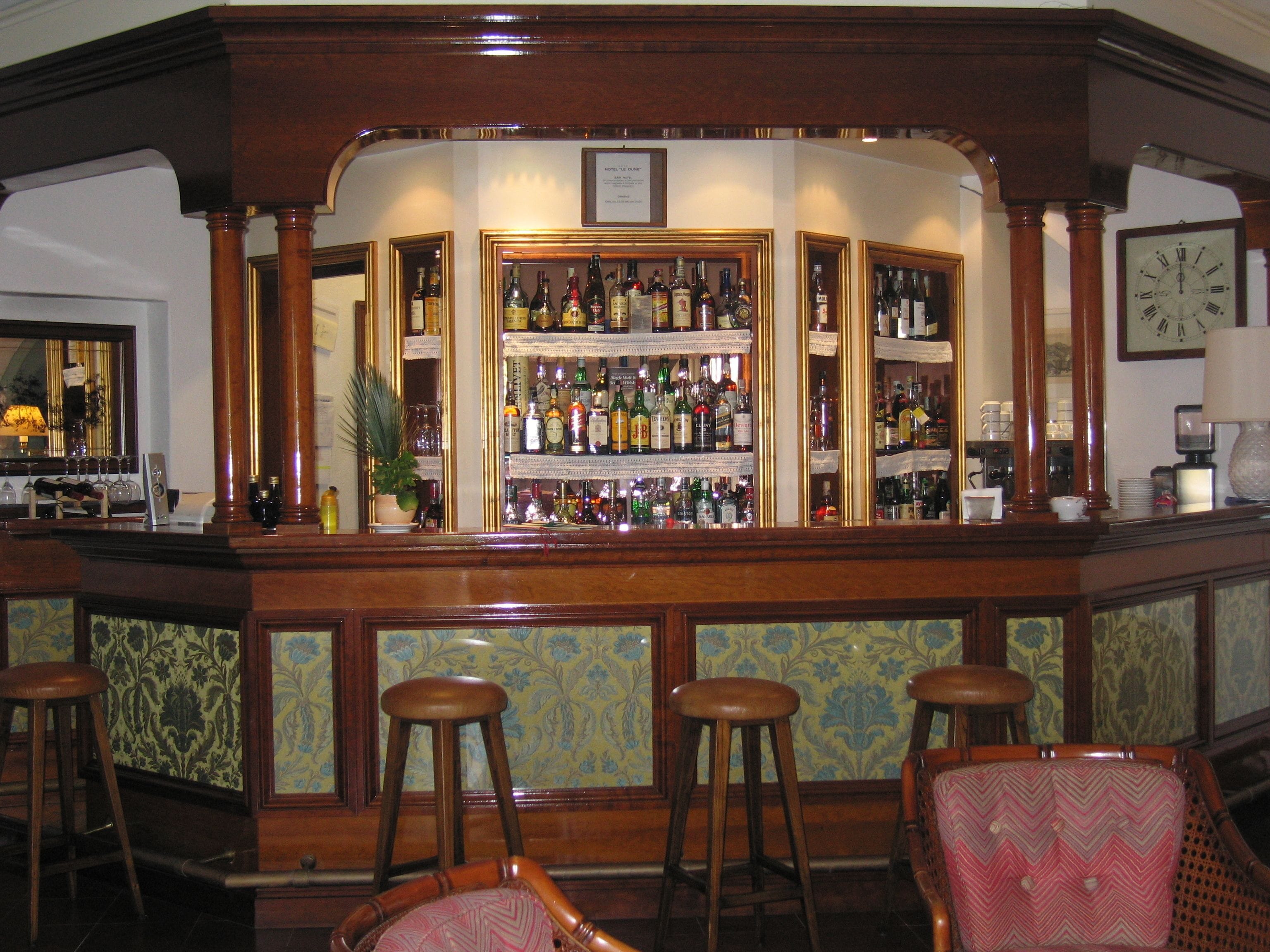 A bar area with a wooden counter, multiple stools, and a variety of liquor bottles.
