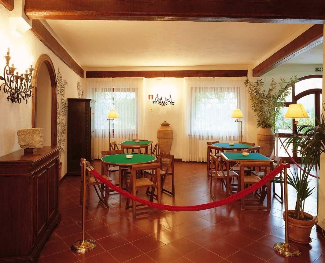 Una habitación con cuatro mesas y sillas verdes, una barrera de cuerda roja y un candelabro.