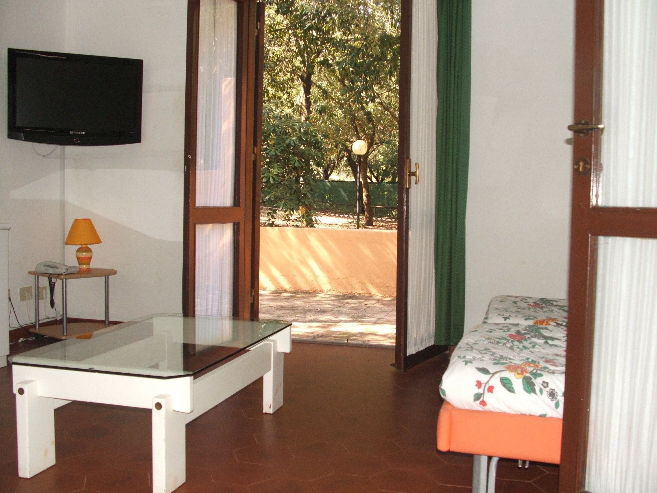 A room with a bed, a table, a lamp, a telephone, and a television on the wall.