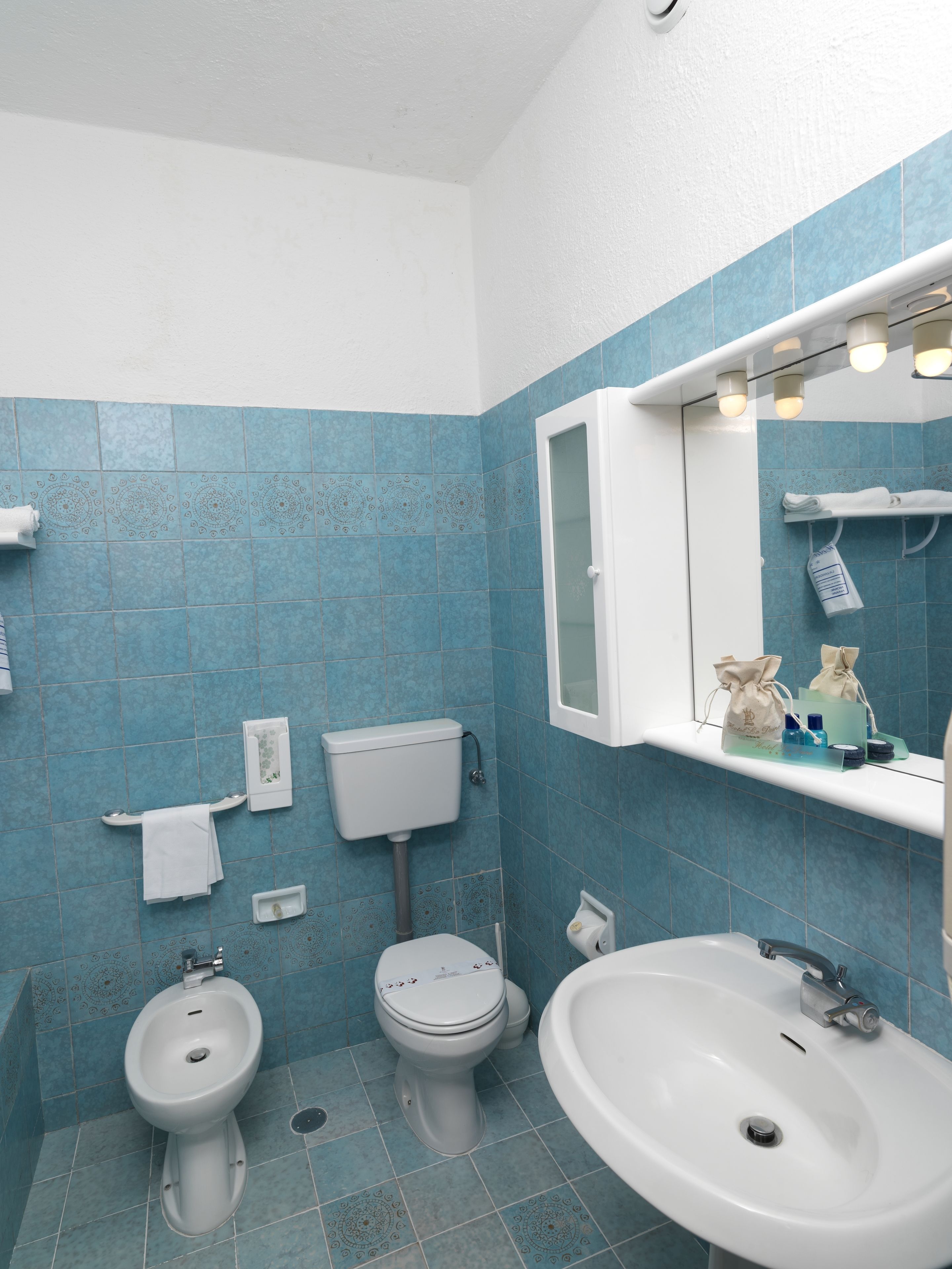 Une salle de bain avec deux toilettes, un bidet, un lavabo et un miroir avec éclairage.