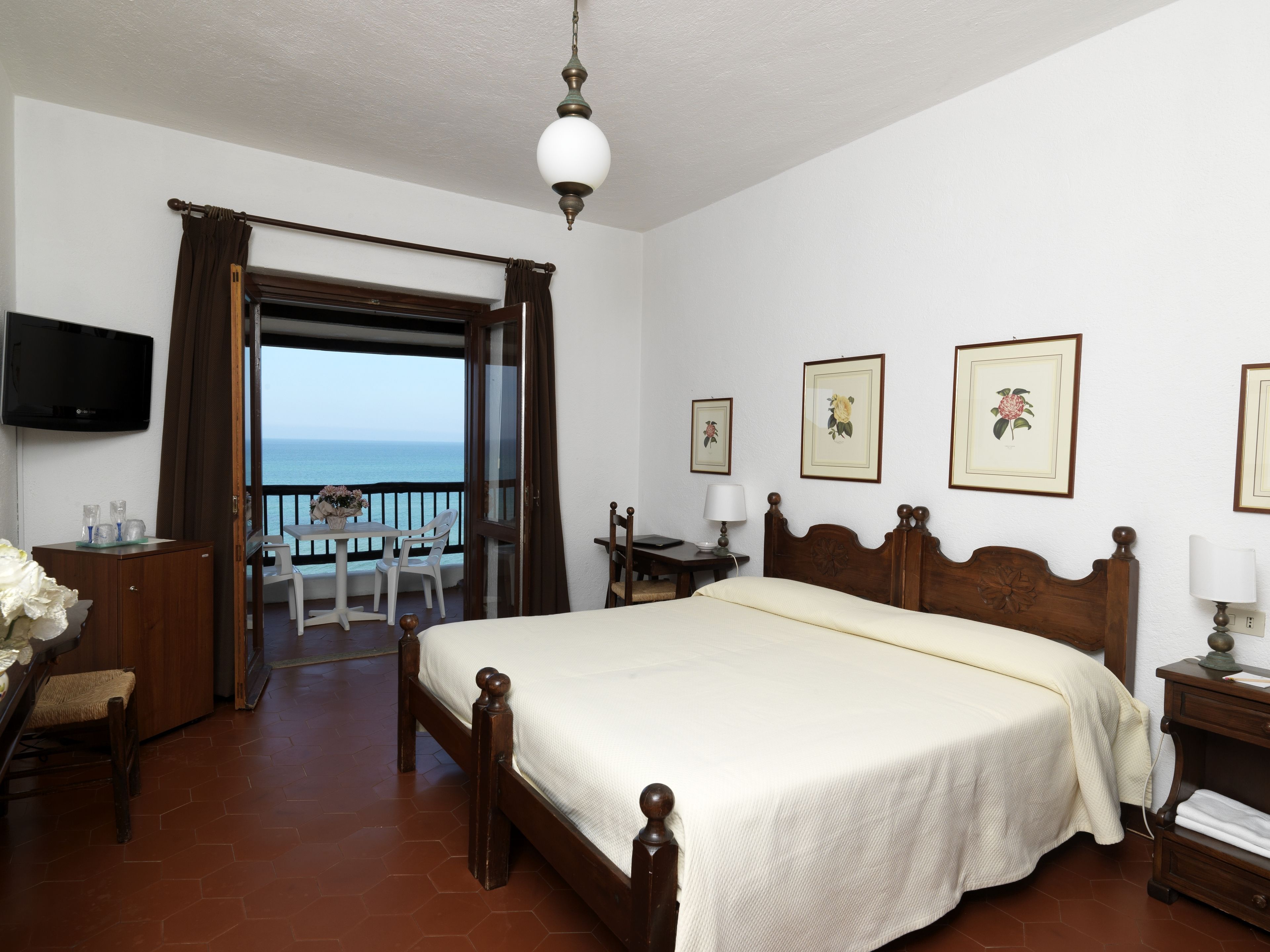 Ein Schlafzimmer mit Bett, Schreibtisch, Stuhl, Fernseher und einem Balkon mit Meerblick.