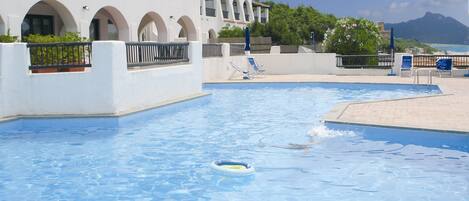 A swimming pool with clear blue water, surrounded by a white building with arched windows and balconies.
