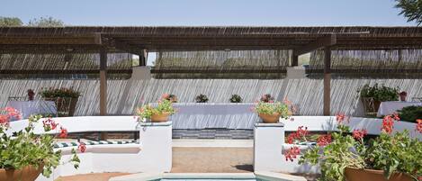 Un área de piscina con una pérgola, mobiliario y plantas en macetas.