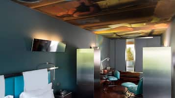 A modern hotel room with a large bed, a desk with a chair, and a view of the outdoors.