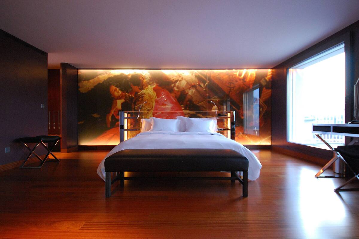 A modern bedroom with a large bed, a desk, and a large window.