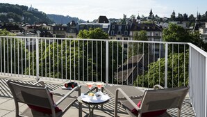 A balcony with two chairs and a table, overlooking a cityscape with buildings and greenery. - The Hotel Luzern, Autograph Collection (Lucerne)