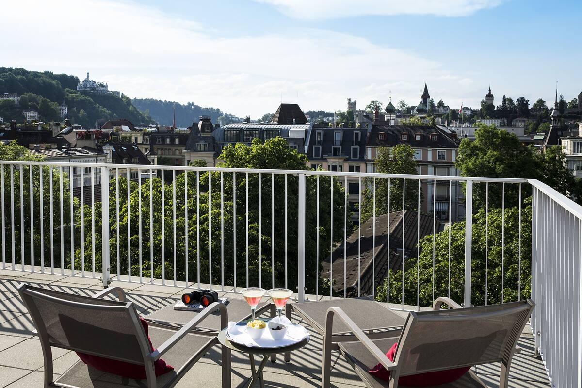 Varanda com duas cadeiras e uma mesa, com vista para um horizonte urbano repleto de edifícios e áreas verdes.