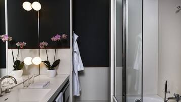 Une salle de bain moderne avec un lavabo blanc, deux orchidées en pot, une cabine de douche en verre et un porte-serviettes.