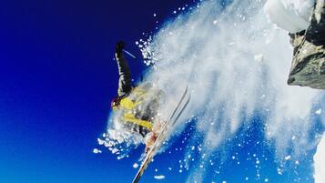 A skier mid-air performing a jump with a snowy mountain landscape in the background.