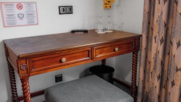 Ein Holztisch mit zwei Schubladen, einer schwarzen Mülleimer und einem kleinen Hocker darunter.