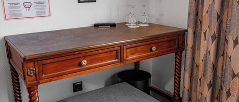 A wooden desk with two drawers, a black trash bin, and a small stool underneath.