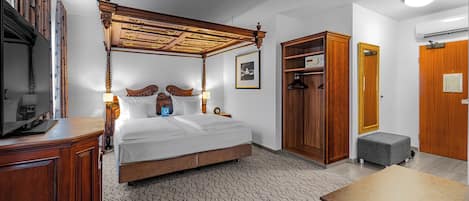 A hotel room with a four-poster bed, a wooden wardrobe, a desk, and a small bench.
