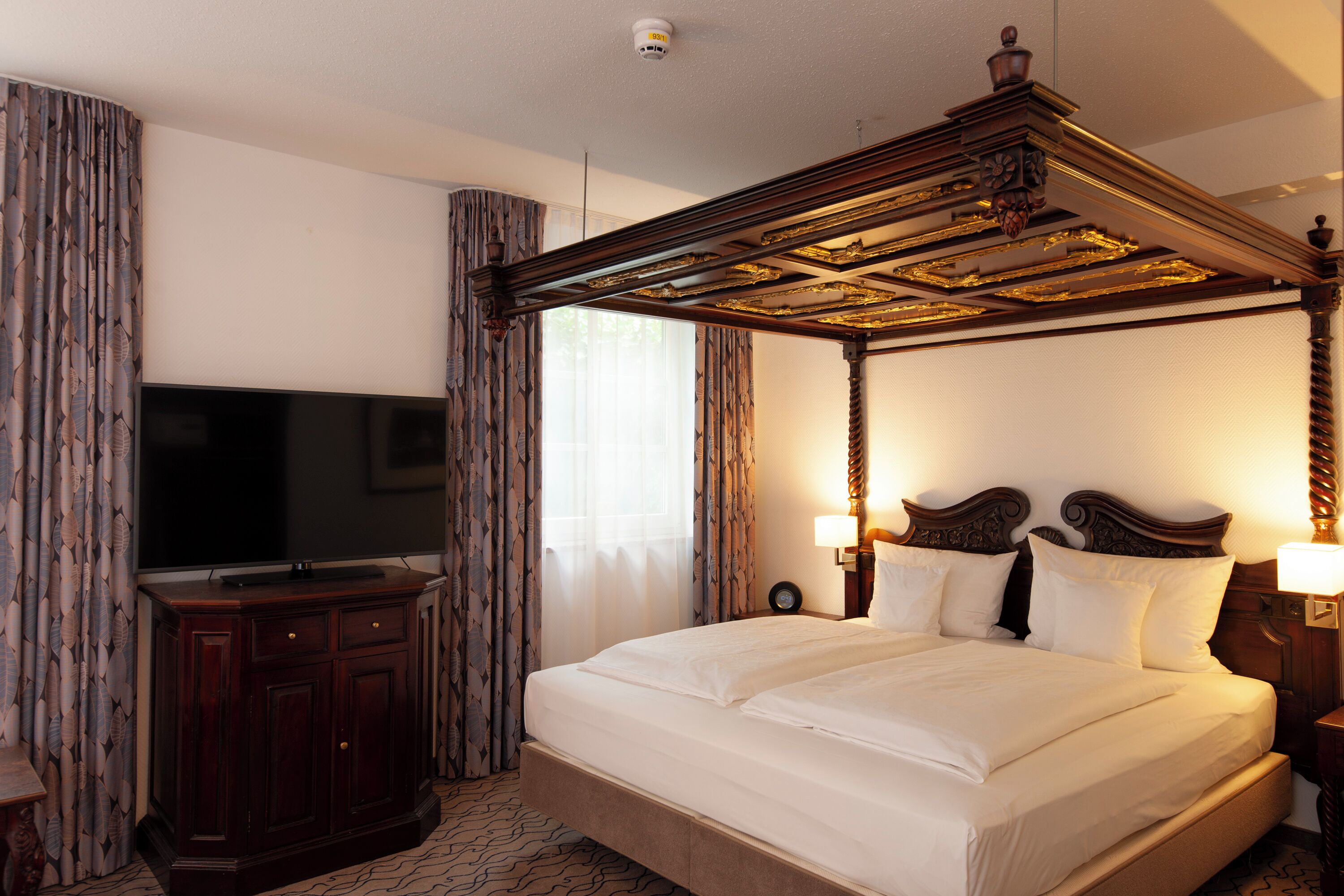 Una habitación de hotel con cama con dosel, televisor de pantalla plana y un armario de madera.