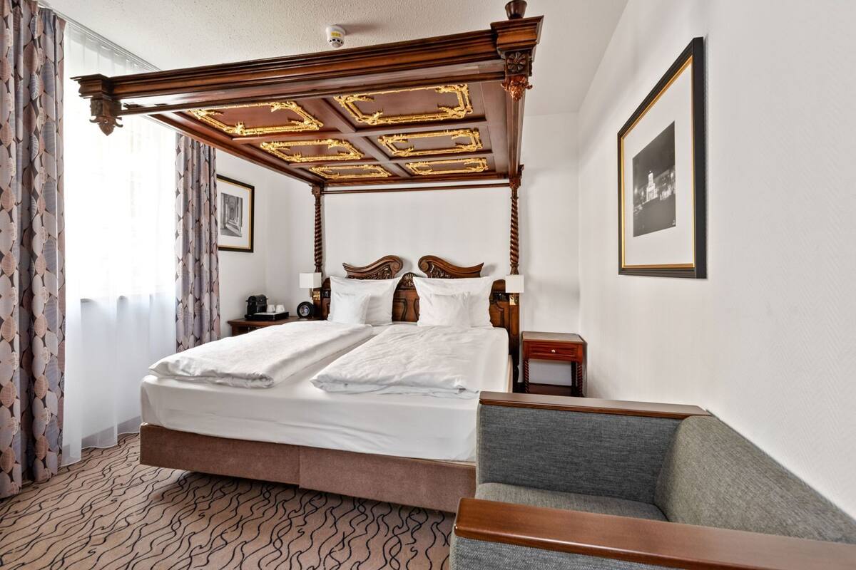 Una cama con dosel, una mesita de noche, una silla y un cuadro en la pared.