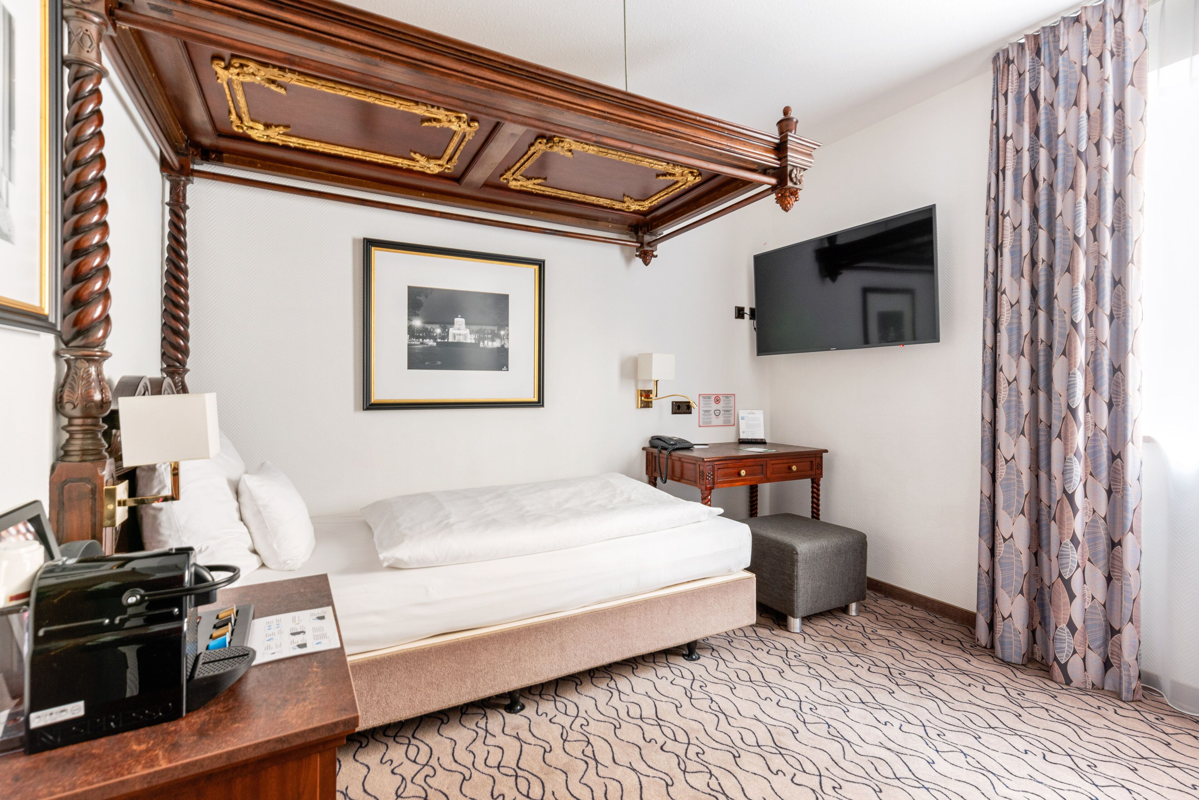 Una habitación de hotel con cama, escritorio, teléfono, televisión y alfombra estampada.