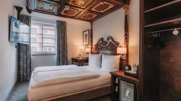 Habitación de hotel con una cama grande, una mesita de noche con lámpara, un armario y un televisor en la pared.