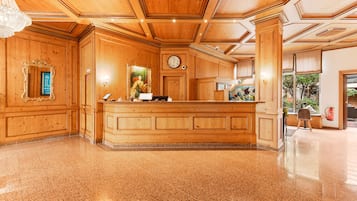 Um balcão de recepção de madeira com um relógio, um espelho e uma placa de identificação em um hall com pisos lustrosos e lambris de madeira.