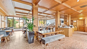 Un comedor amplio con mesas y sillas de madera, una isla central con barra, y ventanas grandes que ofrecen vistas al exterior.