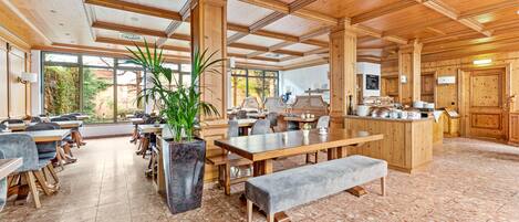 A spacious dining area with wooden tables and chairs, a central island with a bar, and large windows offering views of the outdoors.