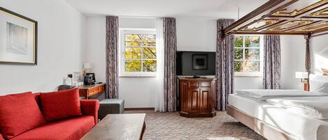 A hotel room with a red sofa, a wooden table, a TV, a wooden cabinet, and a bed with a canopy.