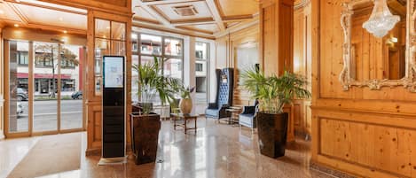 A lobby with wooden paneling, a reception desk, seating area, and a large mirror.