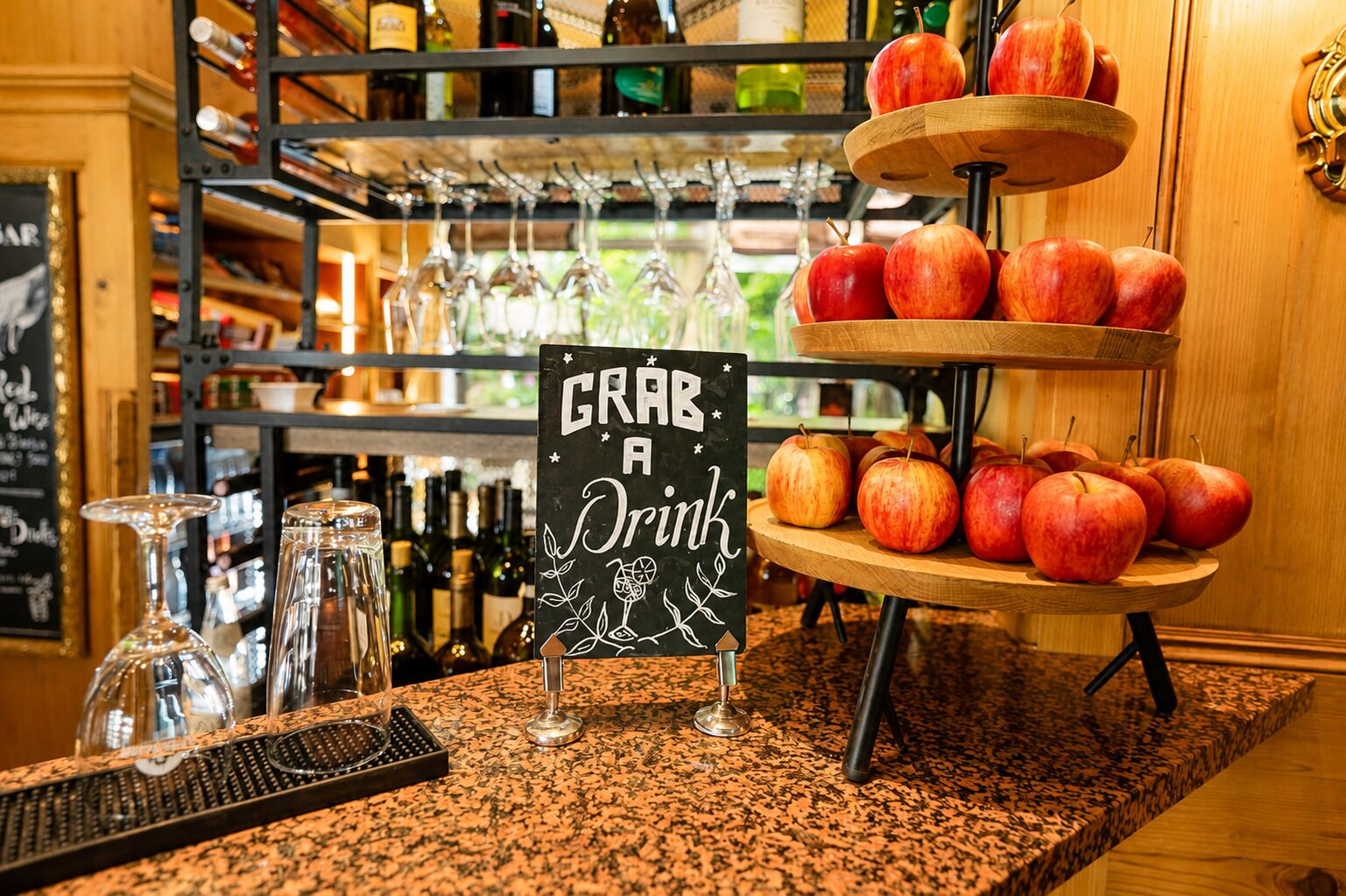 A bar area with a sign that reads 'GRAB A Drink,' a fruit display with apples, and a wine rack in the background.