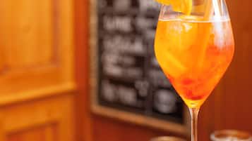 Una copa de cóctel con una rodaja de naranja, un cuenco pequeño de frutos secos y un panel de menú al fondo.