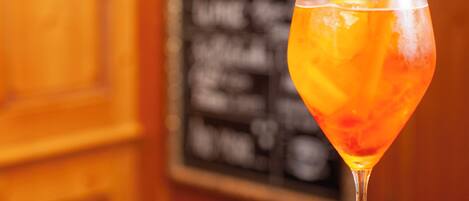 Una copa de cóctel con una rodaja de naranja, un cuenco pequeño de frutos secos y un panel de menú al fondo.