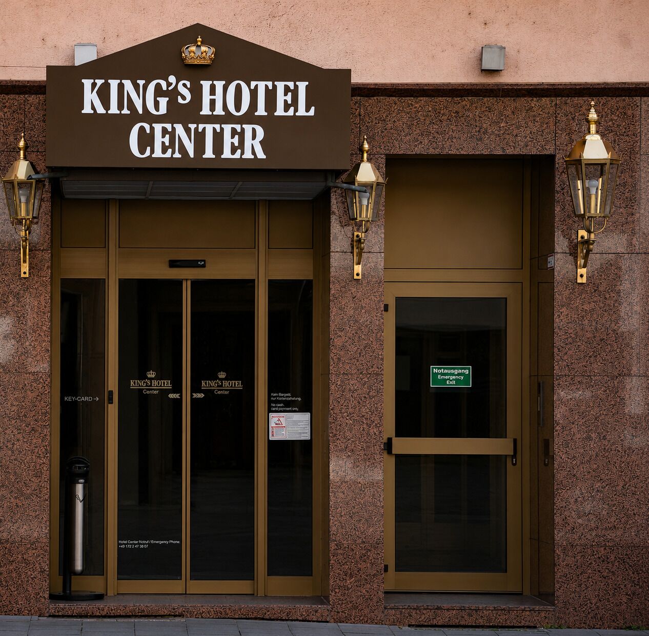 Fachada del Hotel King's Center con un cartel sobre la entrada, dos puertas y dos lámparas en la pared.