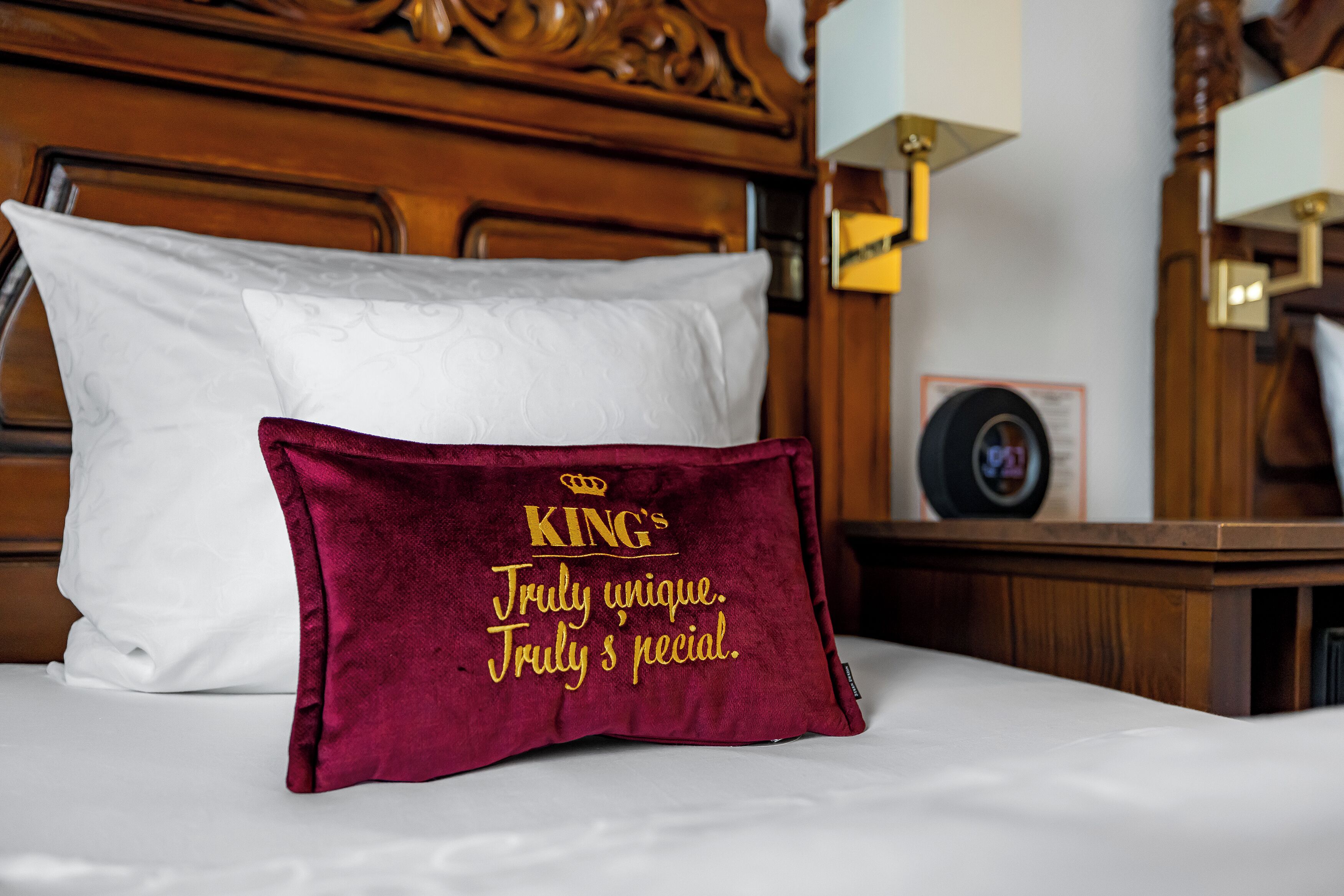 A bed with a white pillow and a red pillow with embroidered text.
