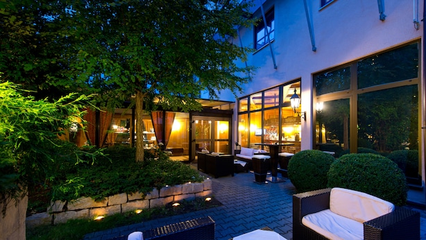 Un espacio al aire libre con patio, muebles de mimbre, una mesa con vela y vista al interior a través de puertas de cristal.