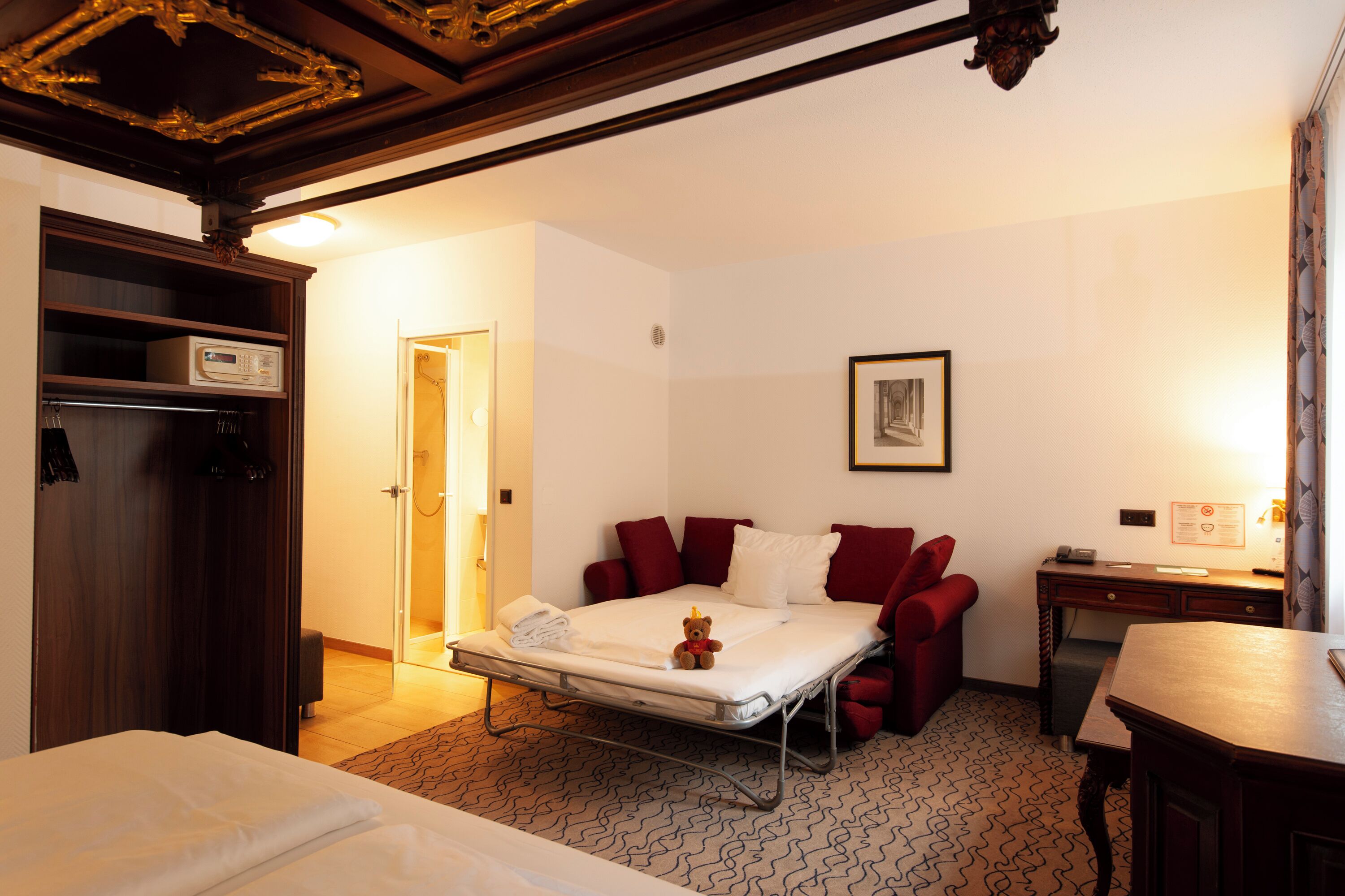 Une chambre d’hôtel avec un lit, un bureau, une chaise, une armoire et une porte.