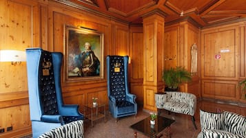 A lobby with wooden paneling, a large portrait, two blue armchairs, a zebra-striped sofa, and a small table with a plant.