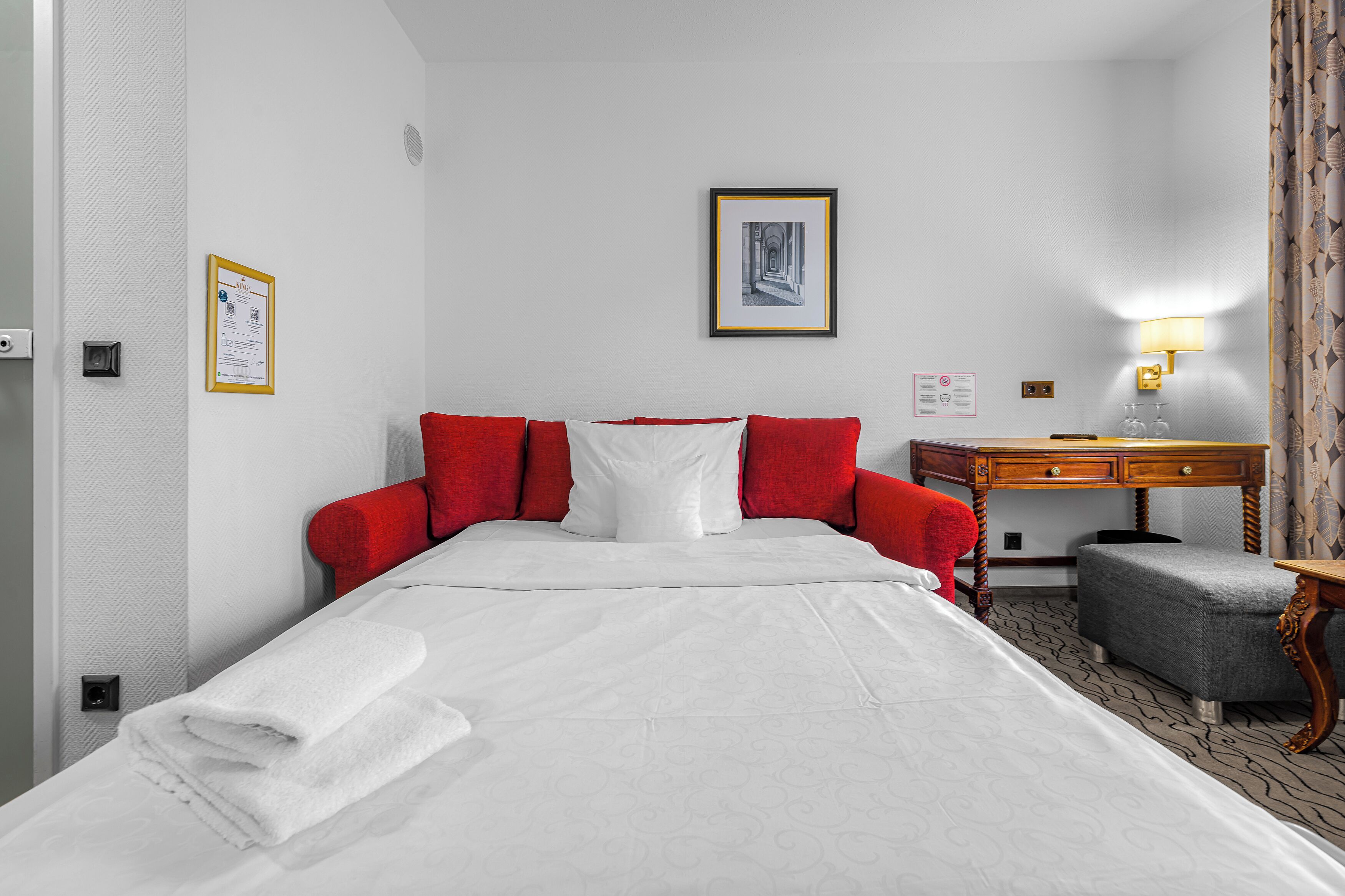 Une chambre d’hôtel avec un lit, un bureau, une chaise, une lampe et un tableau encadré au mur.