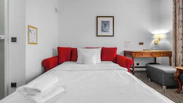 A hotel room with a bed, a desk, a chair, a lamp, and a framed picture on the wall.