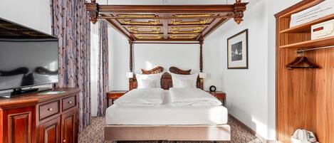 A bedroom with a four-poster bed, a television on a wooden cabinet, patterned curtains, and a framed picture on the wall.