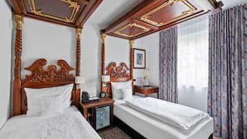 A hotel room with a large bed, a smaller bed, a nightstand, a bedside table, a lamp, a framed picture, and curtains.