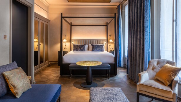 Ein geräumiges Hotelzimmer mit einem Himmelbett, einem runden Couchtisch, einer Couch und einem Sessel.