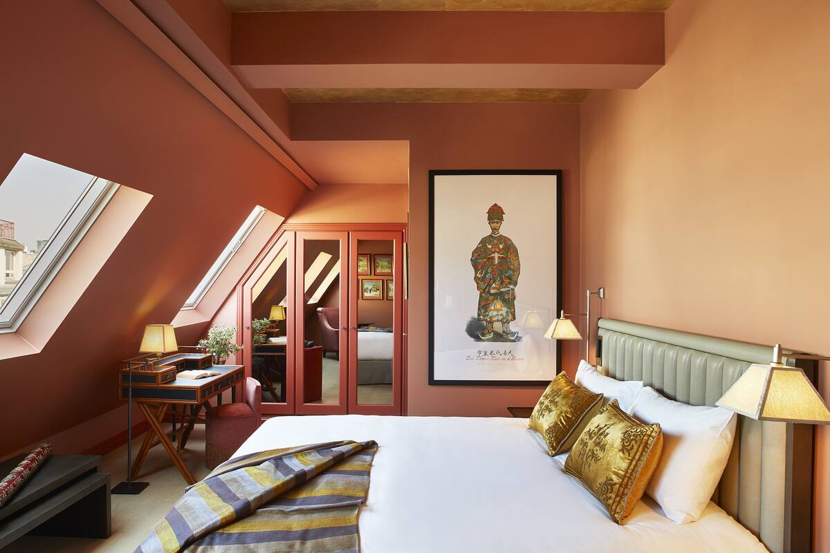 A hotel room with a large bed, a desk, a chair, a wardrobe, and a framed picture on the wall.