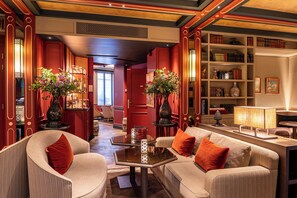 A well-lit, elegantly furnished lounge area with a sofa set, a coffee table, and a bookshelf filled with books and decorative items. - Hôtel de Montesquieu (Paris)